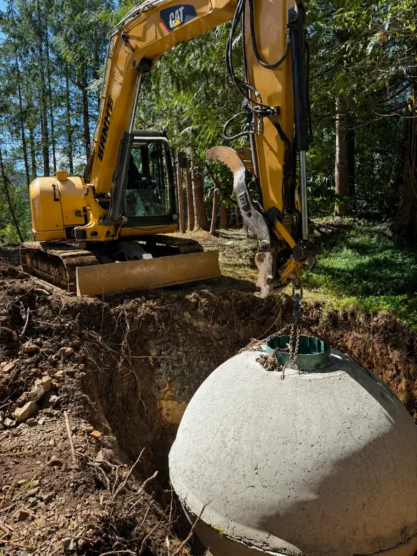 Septic tank being lowered into a wooded excavation during a TTIS gravity septic installation in Port Alberni